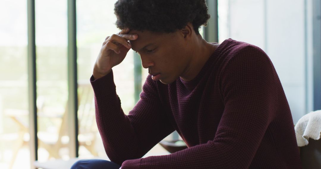 Worried Young Man Sitting Indoors Deep in Thought