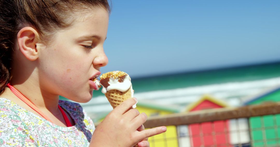 Girl Enjoying Ice Cream by Colorful Beach Huts on a Sunny Day - Free Images, Stock Photos and Pictures on Pikwizard.com