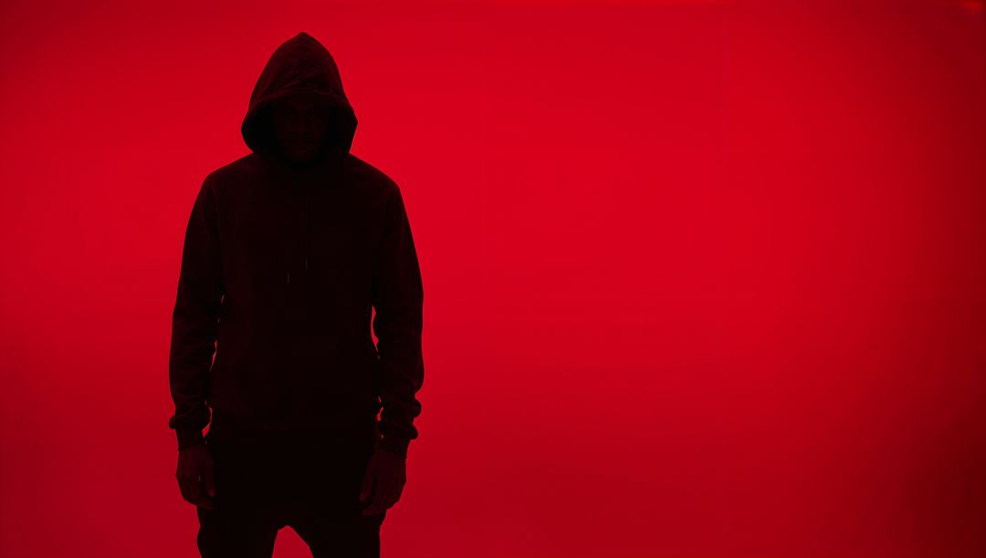 Anonymous Hooded Figure Silhouetted Against Red Background
