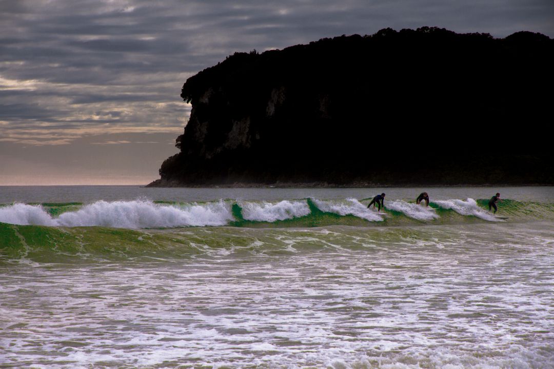 Surfers Riding Waves at Dusk with Scenic Cliff Background - Free Images, Stock Photos and Pictures on Pikwizard.com