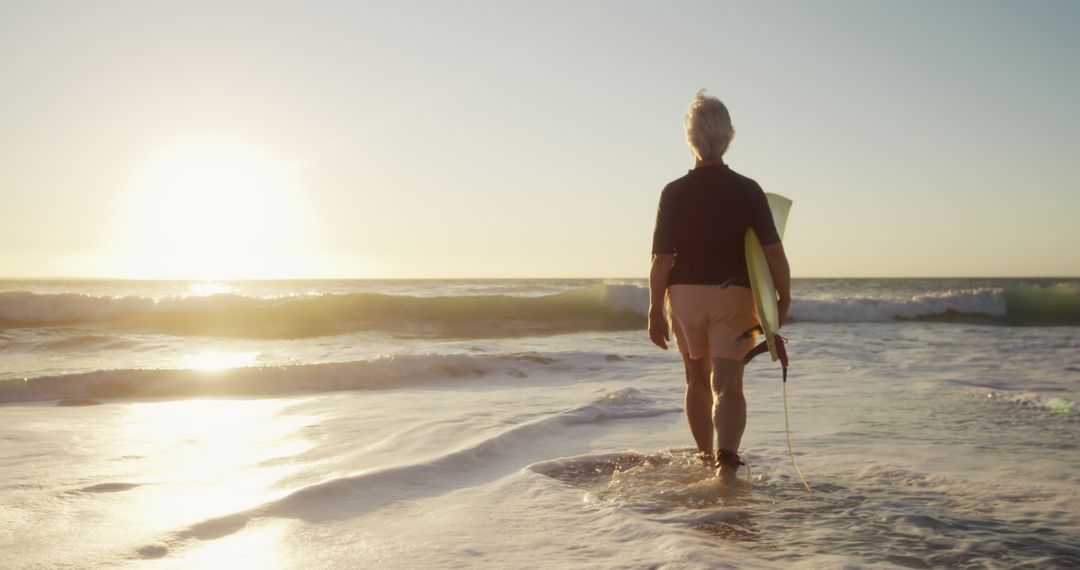 Older man with surfboard walking into ocean at sunrise - Free Images, Stock Photos and Pictures on Pikwizard.com