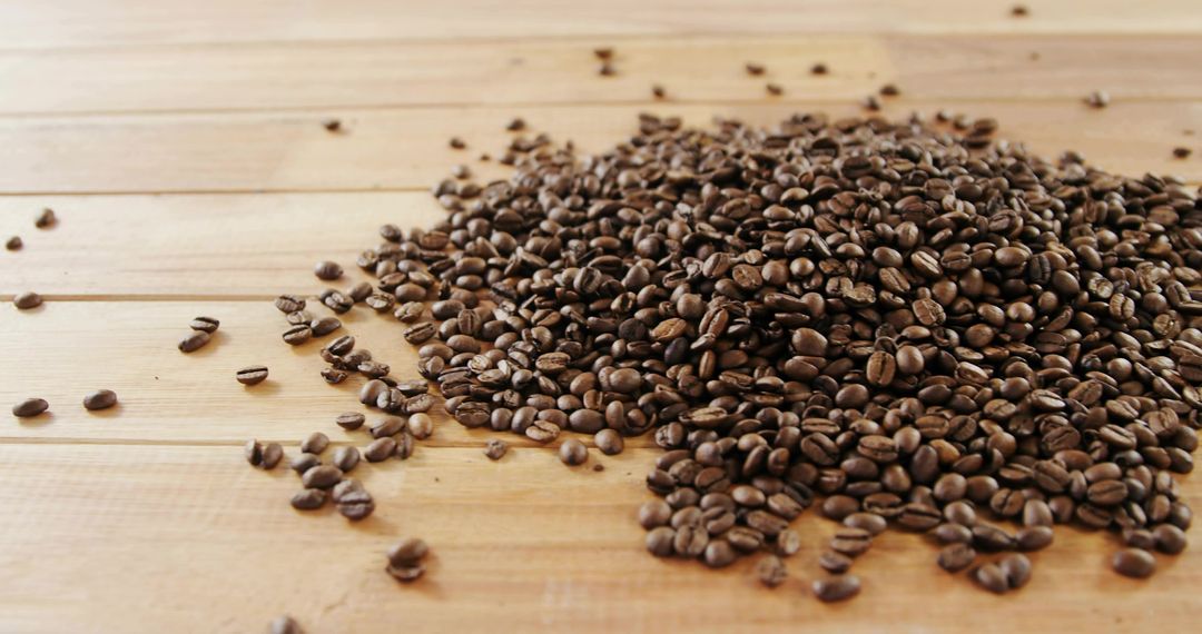 Heaping dark roasted coffee beans spilling across rustic wooden countertop