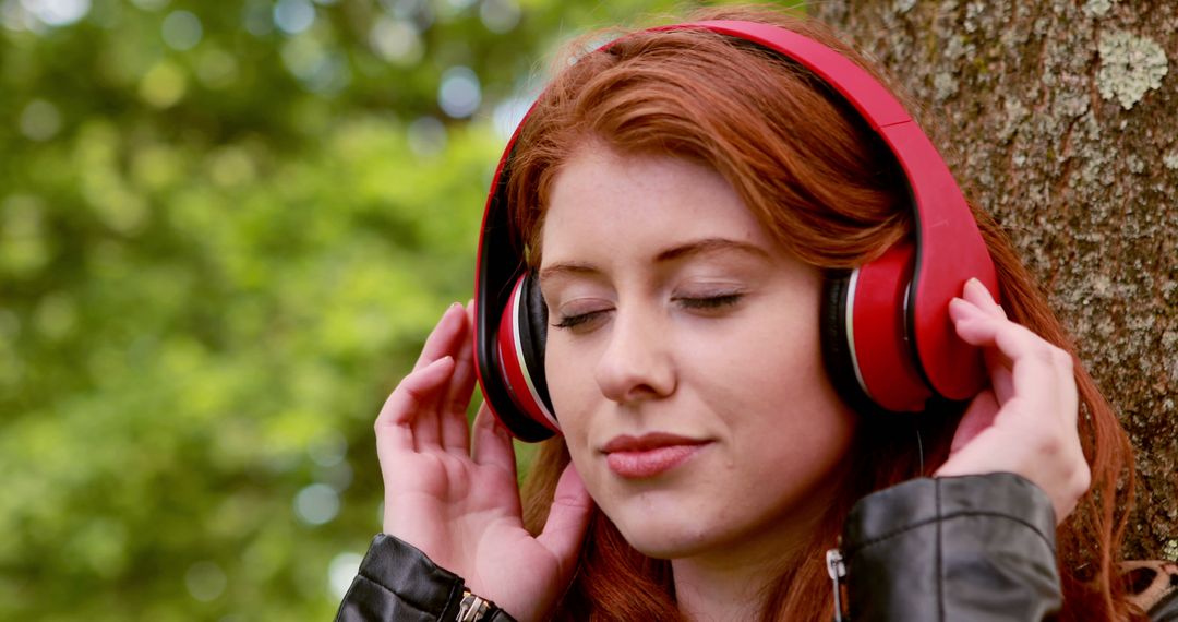 Pretty redhead listening to music in the park on a sunny day - Free Images, Stock Photos and Pictures on Pikwizard.com