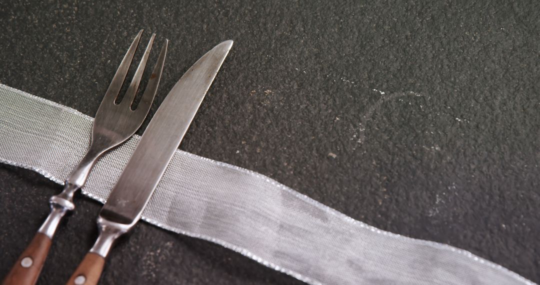 A fork and knife are placed next to each other on a dark textured surface, with copy space - Free Images, Stock Photos and Pictures on Pikwizard.com