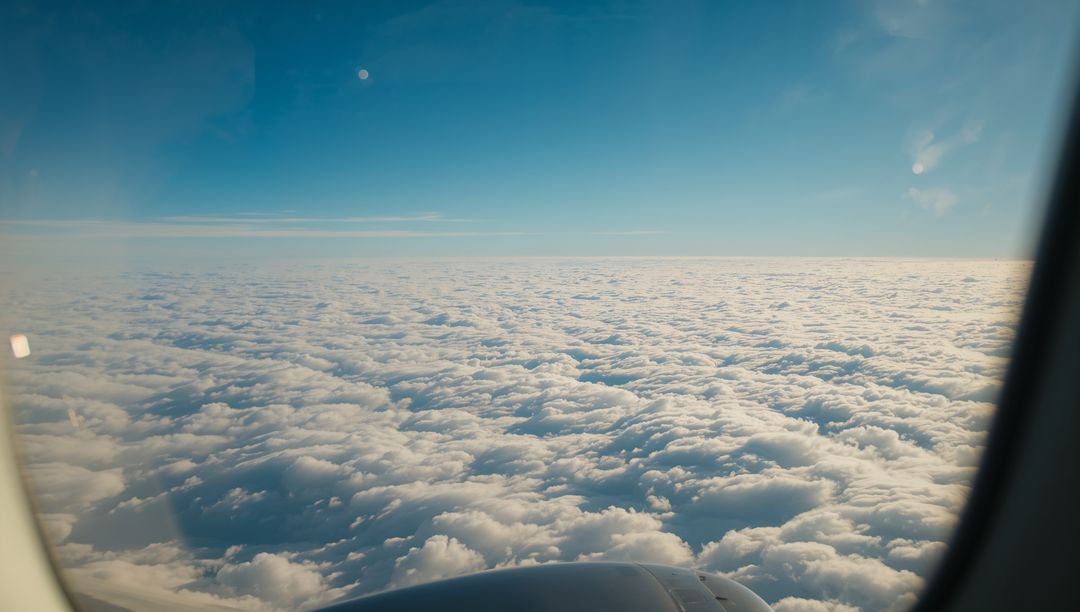 Revealing rolling cloud deck from airplane window with engine and sunlit horizon above clouds