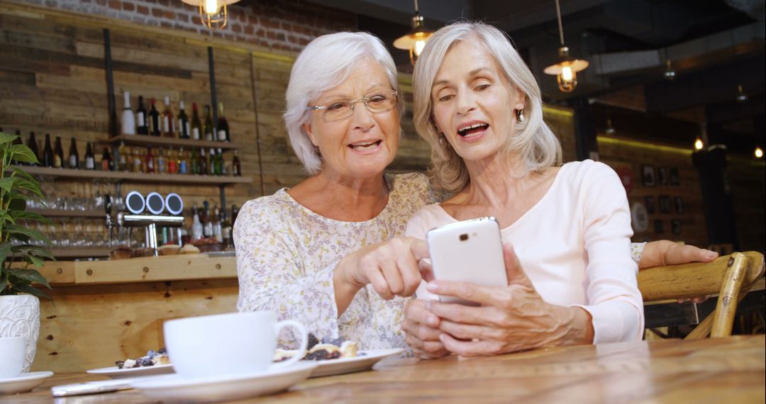 Two Senior Women Enjoying Time Together Looking at Smartphone in Cozy Cafe - Free Images, Stock Photos and Pictures on Pikwizard.com