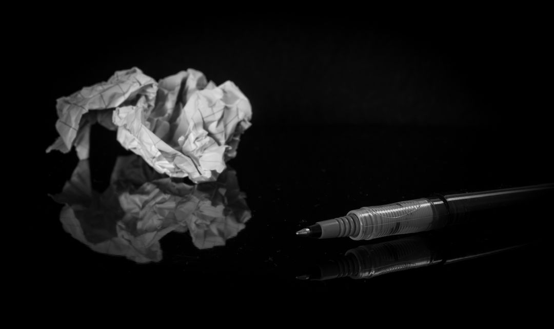 Crumpled Paper and Pen on Reflective Surface in Monochrome