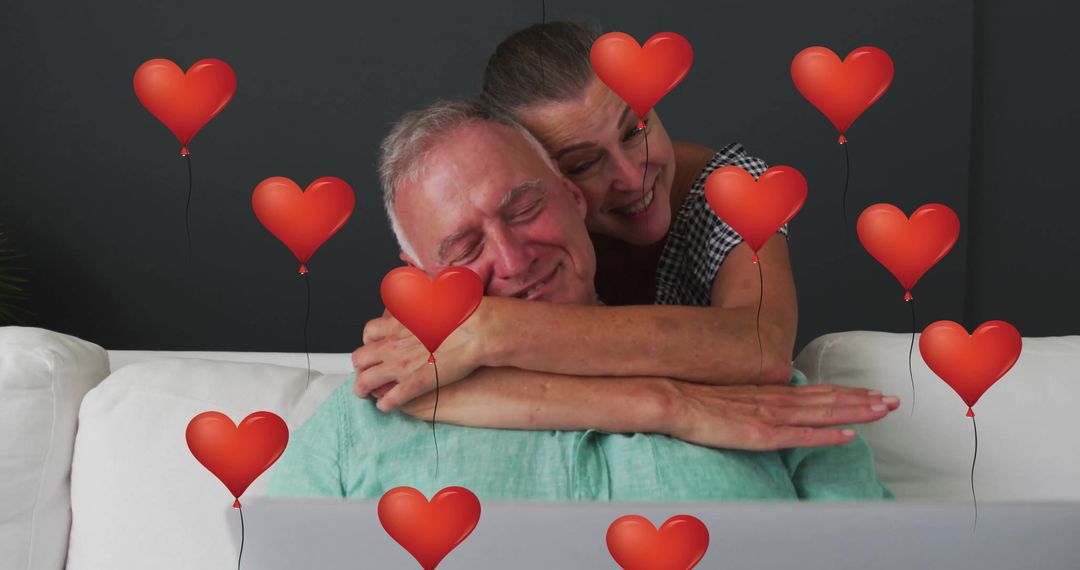 Senior Couple Embracing With Heart Balloons and Laptop
