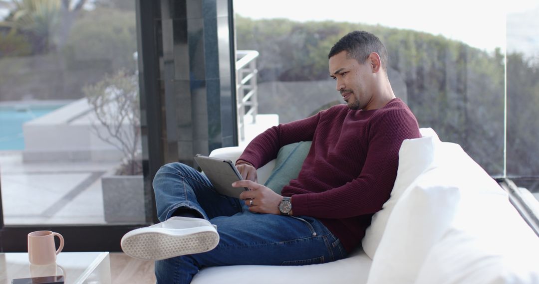 Man Relaxing on Modern Sofa with Tablet Near Large Windows
