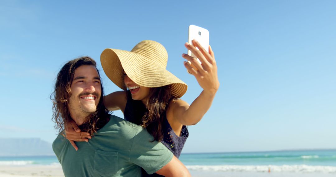 Joyful Couple Piggybacking on Beach Taking Selfie - Free Images, Stock Photos and Pictures on Pikwizard.com