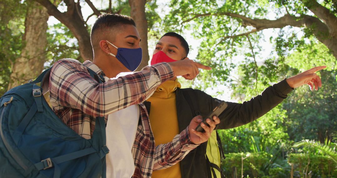 Friends Navigating with Smartphone and Backpacks in Park during Pandemic