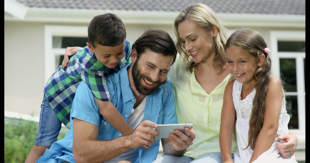 Happy Family Laughing and Looking at Smartphone in Sunny Backyard - Free Images, Stock Photos and Pictures on Pikwizard.com