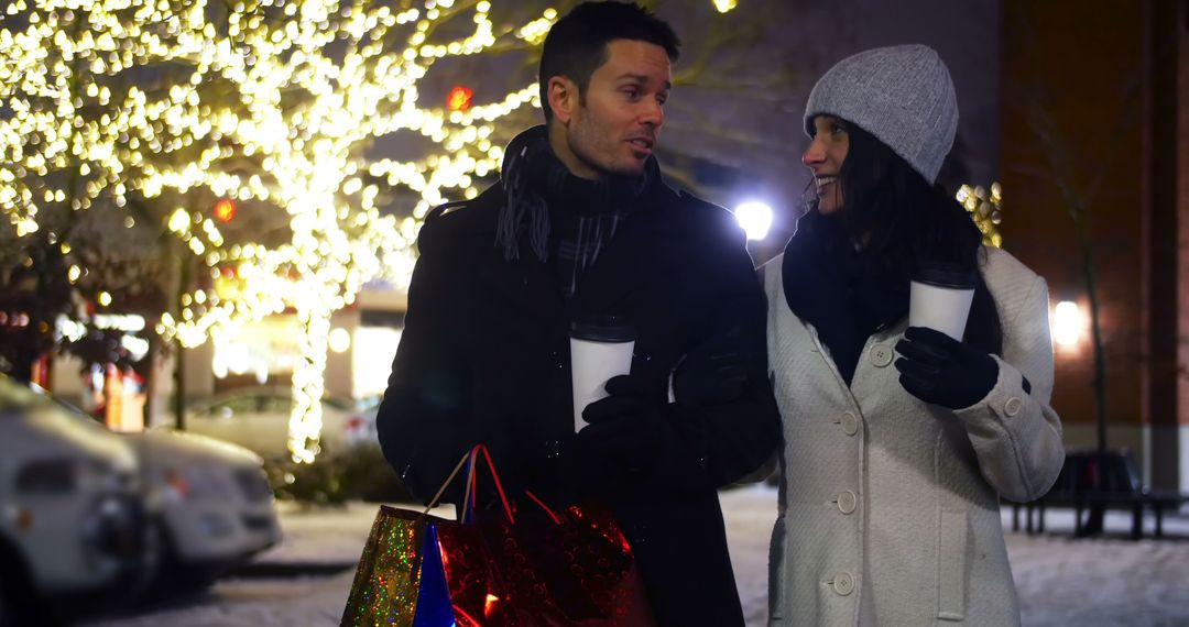 Couple Enjoying Winter Night Walk with Hot Drinks and Shopping Bags - Free Images, Stock Photos and Pictures on Pikwizard.com