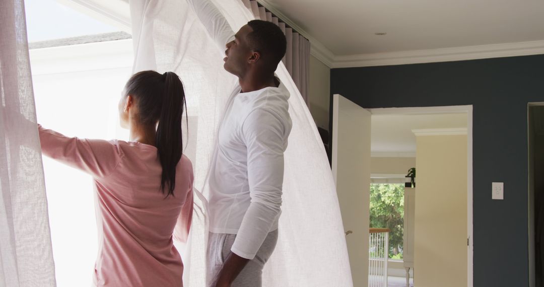 Image of happy diverse couple drawing curtains and looking out of window at home, with copy space - Free Images, Stock Photos and Pictures on Pikwizard.com
