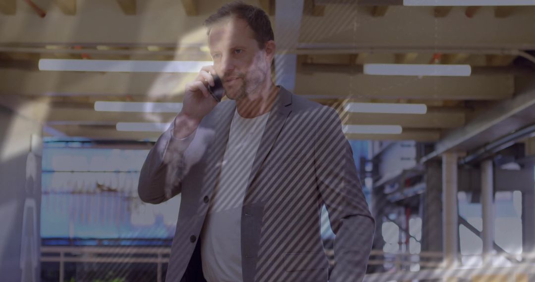 Businessman walking in transit atrium talking on smartphone, reflective glass overlays