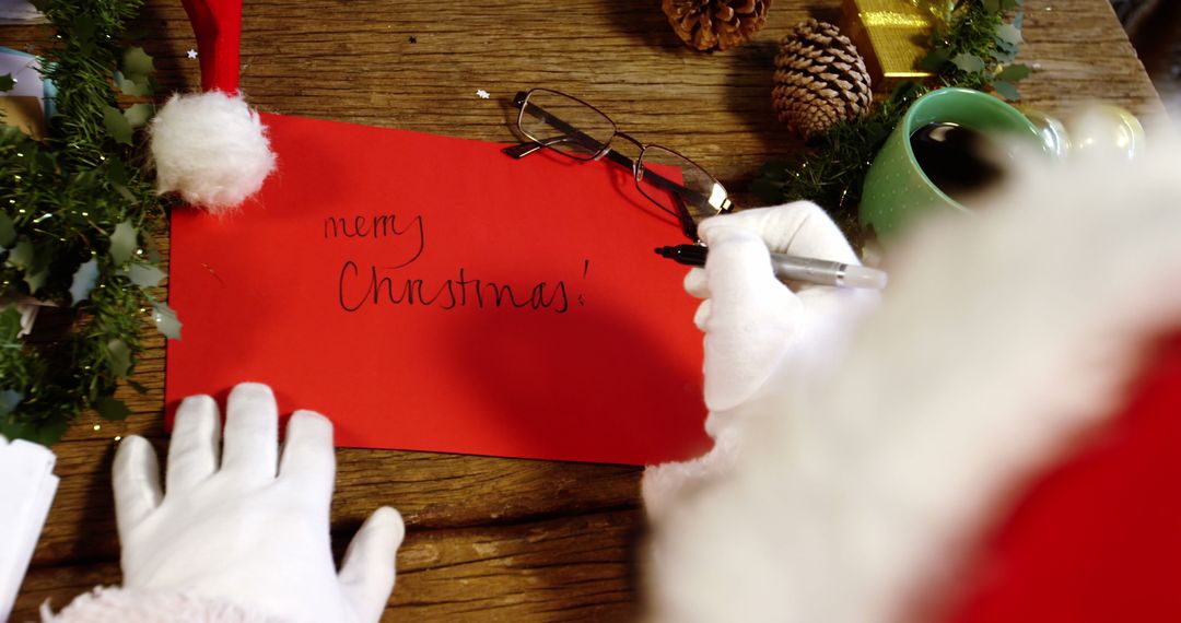 Santa Claus Writing Merry Christmas Card on Wooden Table - Free Images, Stock Photos and Pictures on Pikwizard.com