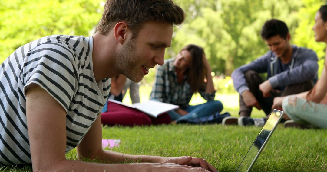 Young Man Using Laptop in Park with Friends Relaxing Outdoors - Free Images, Stock Photos and Pictures on Pikwizard.com