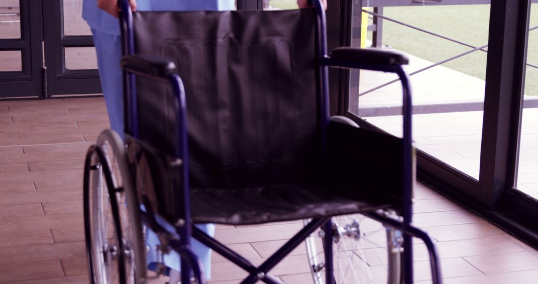 Healthcare Worker Pushing Empty Wheelchair in Hospital Corridor - Free Images, Stock Photos and Pictures on Pikwizard.com