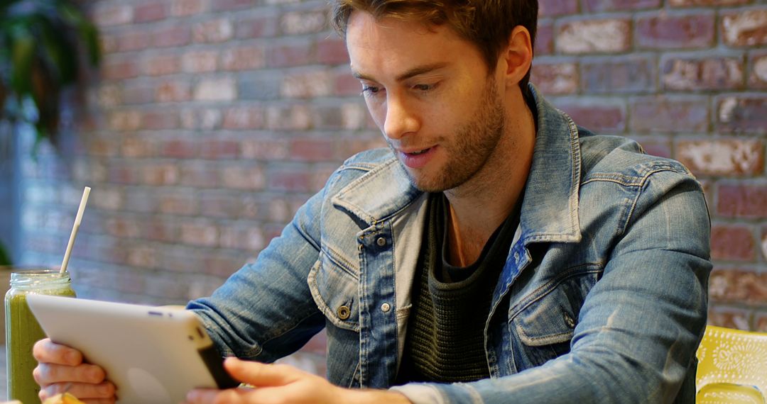 Young Man Using Tablet in Café with Brick Wall Background - Free Images, Stock Photos and Pictures on Pikwizard.com