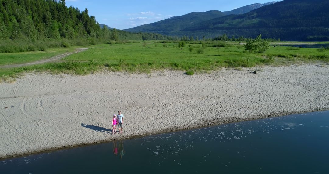 Couple Standing on Serene Sandy Beach Near Forest and Mountain Range - Free Images, Stock Photos and Pictures on Pikwizard.com