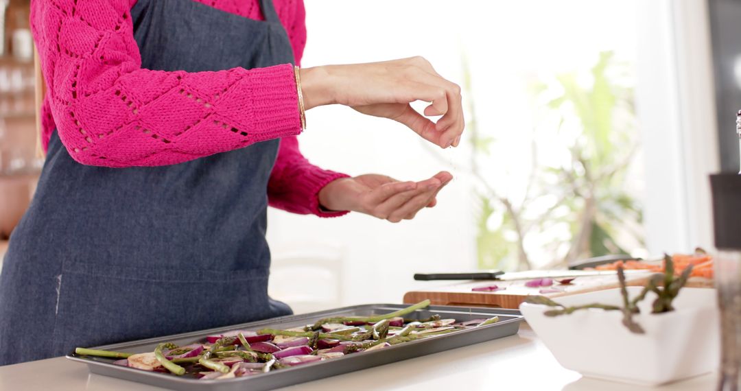 Person in Pink Sweater Sprinkling Herbs on Fresh Vegetables on Baking Tray - Free Images, Stock Photos and Pictures on Pikwizard.com