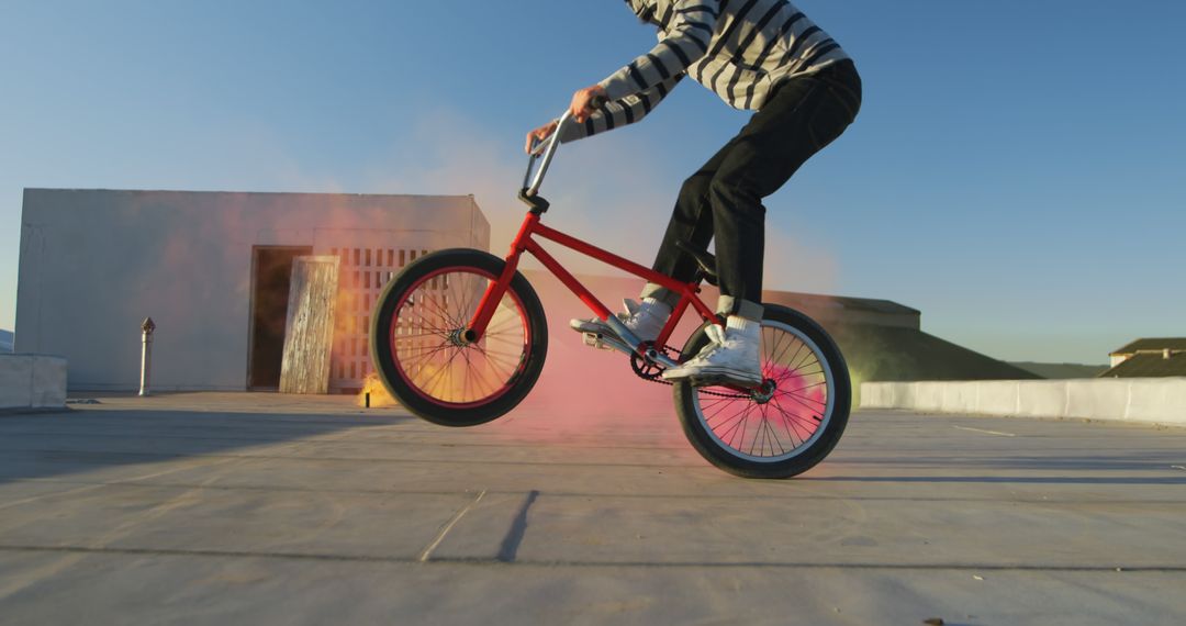 A young man performs BMX stunts on a warehouse rooftop amidst vibrant smoke plumes. - Free Images, Stock Photos and Pictures on Pikwizard.com