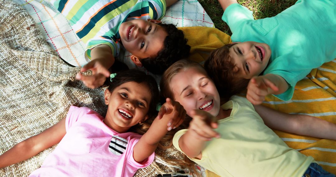 Diverse Happy Children Lying On Blanket Pointing at Camera in Outdoor Park - Free Images, Stock Photos and Pictures on Pikwizard.com