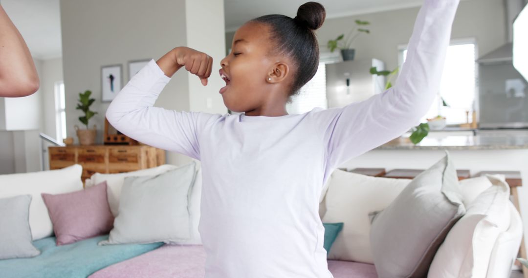 Excited African American Girl Flexing Muscles in Living Room - Free Images, Stock Photos and Pictures on Pikwizard.com