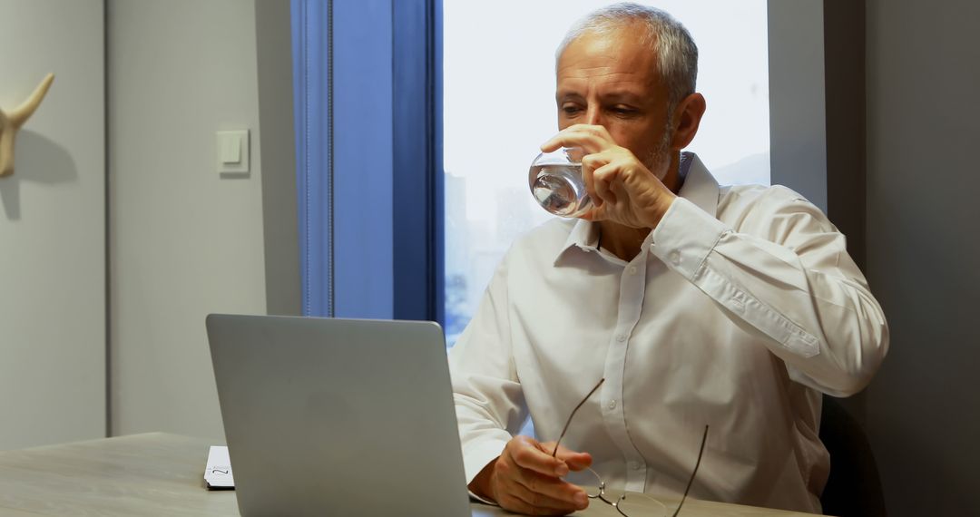 Senior Man Drinking Water While Working on Laptop at Office Desk - Free Images, Stock Photos and Pictures on Pikwizard.com