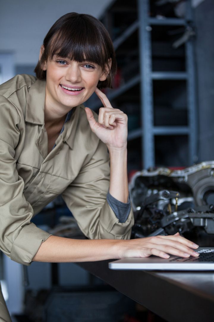 Smiling Female Mechanic Working on Laptop in Garage Setting