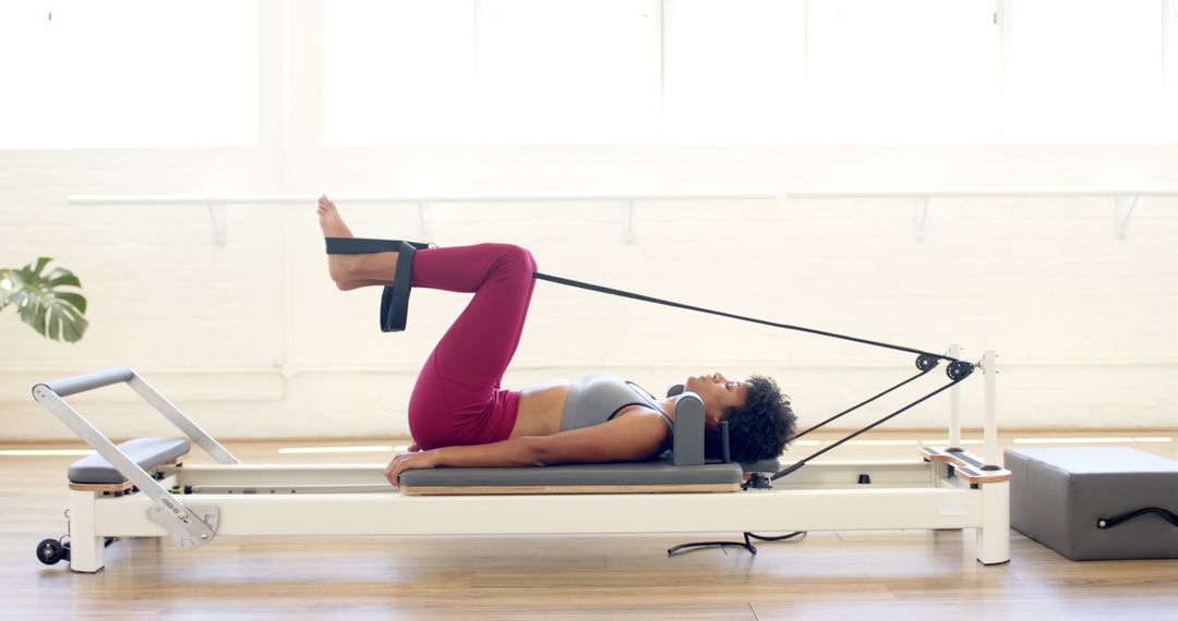 Focused Woman Practicing Pilates on Reformer in Bright Studio