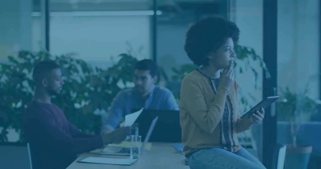 Pensive professional holding tablet while collaborating with team in modern office meeting