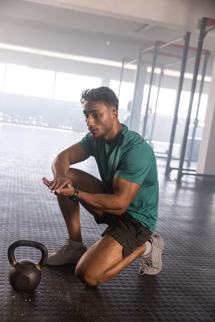 Athlete Kneeling with Kettlebell Chalking Hands in Gym