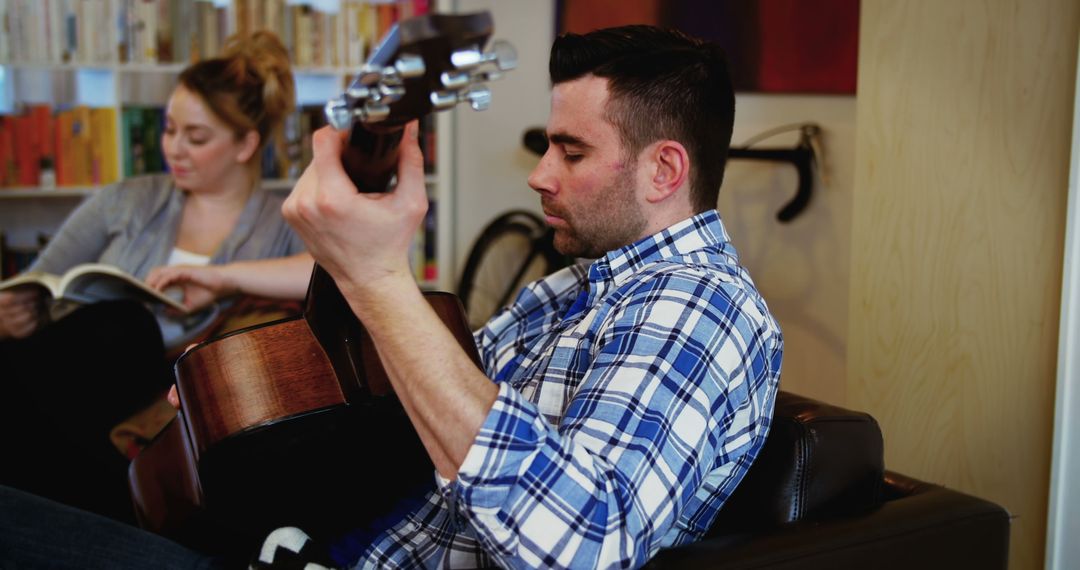 Man Playing Guitar While Woman Reads Book in Cozy Home Setting