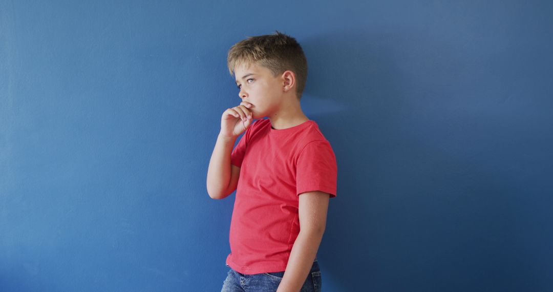 Thoughtful Young Boy Standing Against Blue Wall in Red Shirt - Free Images, Stock Photos and Pictures on Pikwizard.com