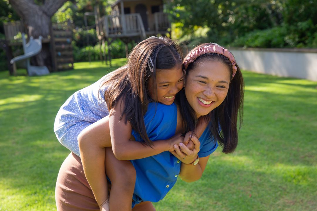 Mother Giving Daughter Piggyback Ride in Sunny Backyard