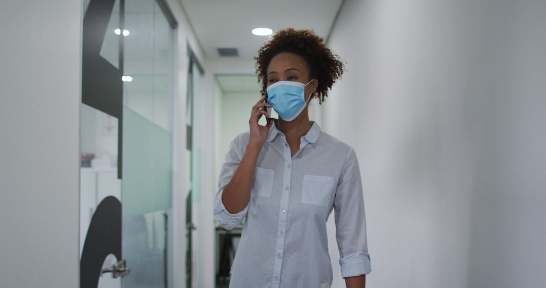 Woman Wearing Face Mask Talking on Phone in Office Corridor - Free Images, Stock Photos and Pictures on Pikwizard.com