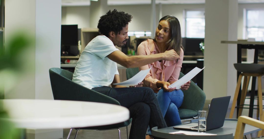 Colleagues collaborating over documents in modern open-plan office lounge with laptop