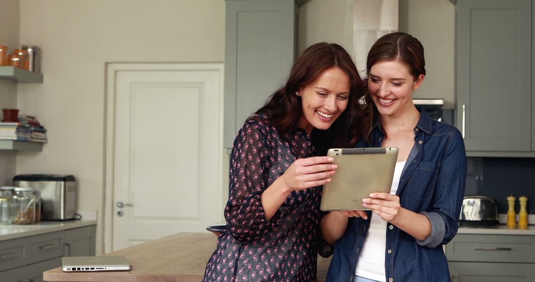 Two Young Women Smiling and Using Tablet in Modern Kitchen - Free Images, Stock Photos and Pictures on Pikwizard.com