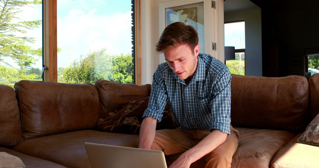 Young Man Using Laptop on Sofa in Modern Living Room with Natural Light - Free Images, Stock Photos and Pictures on Pikwizard.com