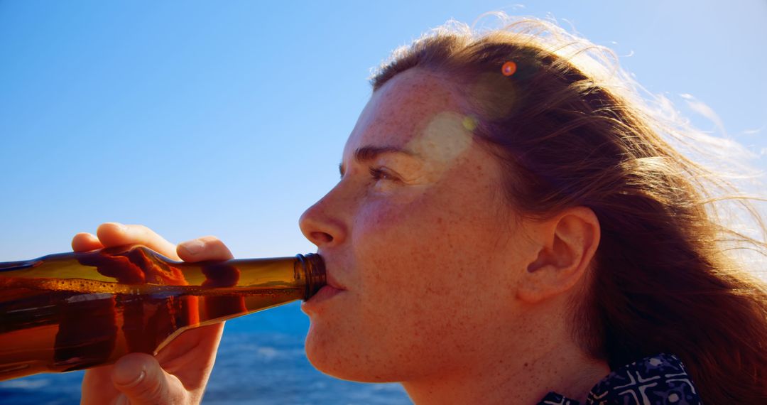 Young Woman Drinking Beer by Ocean on Sunny Day - Free Images, Stock Photos and Pictures on Pikwizard.com