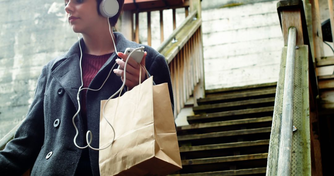 Young Woman Listening to Music While Carrying Shopping Bag on Urban Staircase - Free Images, Stock Photos and Pictures on Pikwizard.com