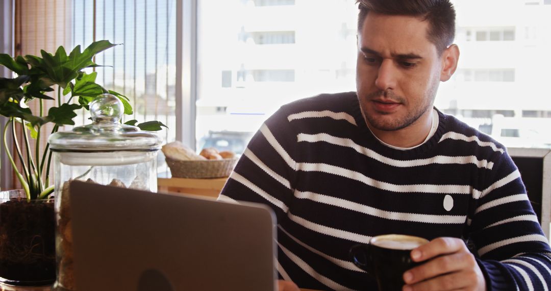 Man Studying Laptop in Coffee Shop While Holding Cup of Coffee