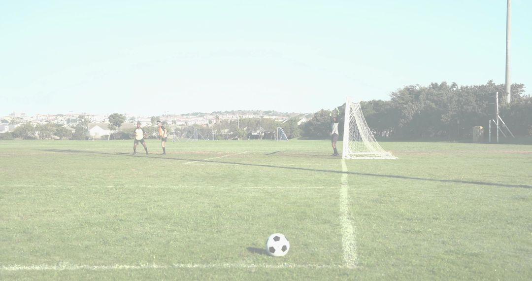 Youth soccer players walking toward goal with soccer ball in foreground on sunny field