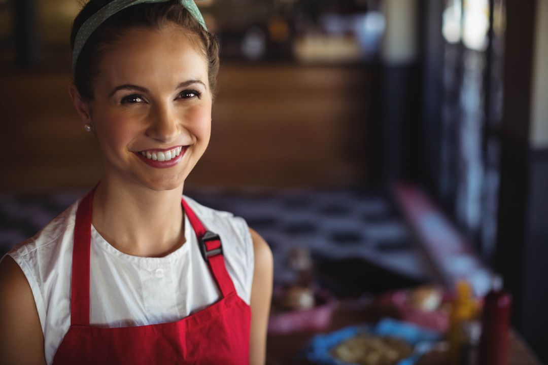 Smiling Female Barista in Red Apron Behind Counter