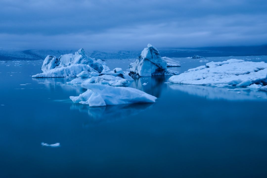 Drifting Icebergs in Blue Glacial Lagoon at Twilight Reflecting Calm Water and Moody Sky