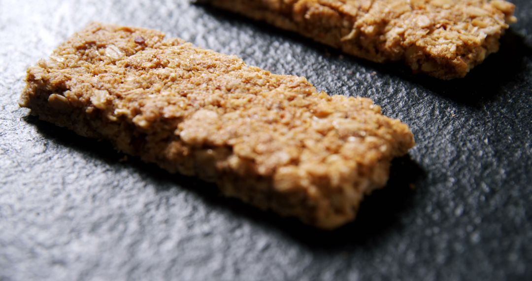 Two oatmeal bars are placed on a dark textured surface, offering a healthy snack option - Free Images, Stock Photos and Pictures on Pikwizard.com