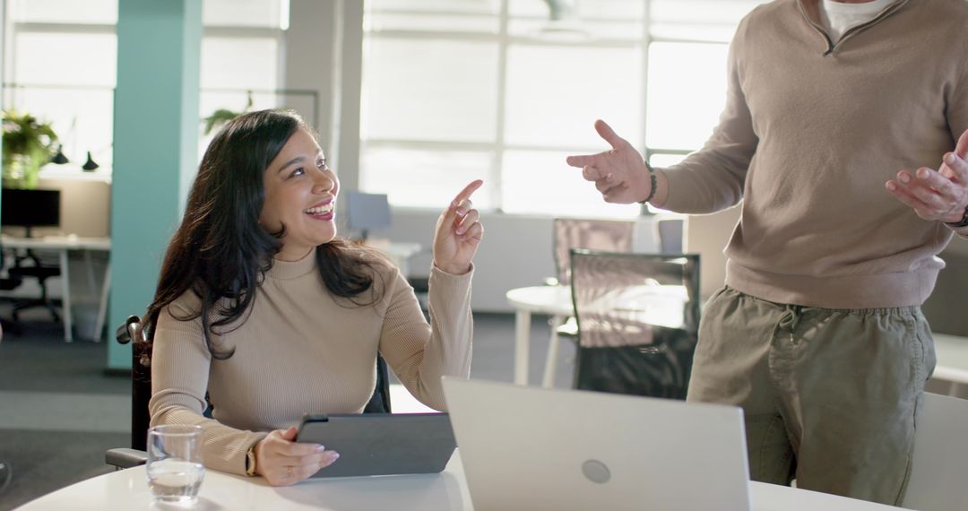 Smiling diverse coworkers collaborating over tablet in bright modern open-plan office daylight