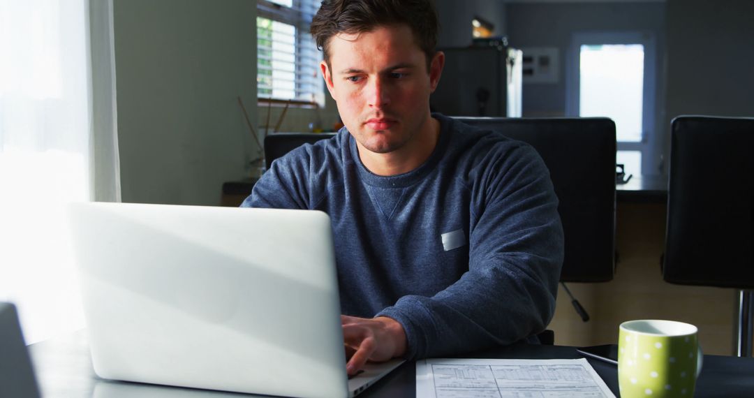 Young Man Working on Laptop at Home With Papers and Coffee Mug - Free Images, Stock Photos and Pictures on Pikwizard.com