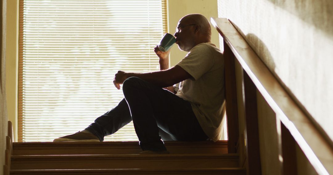 Man Sitting on Staircase Drinking Coffee Reflecting by Window Light - Free Images, Stock Photos and Pictures on Pikwizard.com